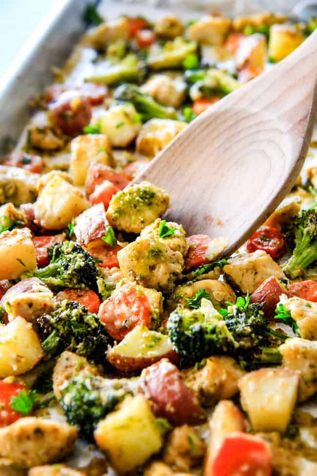 Sheet Pan Parmesan Pesto Chicken with Potatoes, Broccoli and Carrots on a pan and wood spoon.