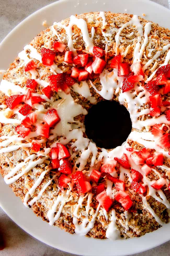 Strawberry Cream Cheese STUFFED Sour Cream Coffee Cake - this is the best strawberry coffee cake ever! the INCREDIBLY creamy cheesecake-like cream cheese filling and strawberries all topped with Coconut Pecan Streusel and Lemon Drizzle is OUT OF THIS WORLD! I can't say enough good things about this coffee cake! Top view of easy Cream cheese Coffee Cake on a white plate