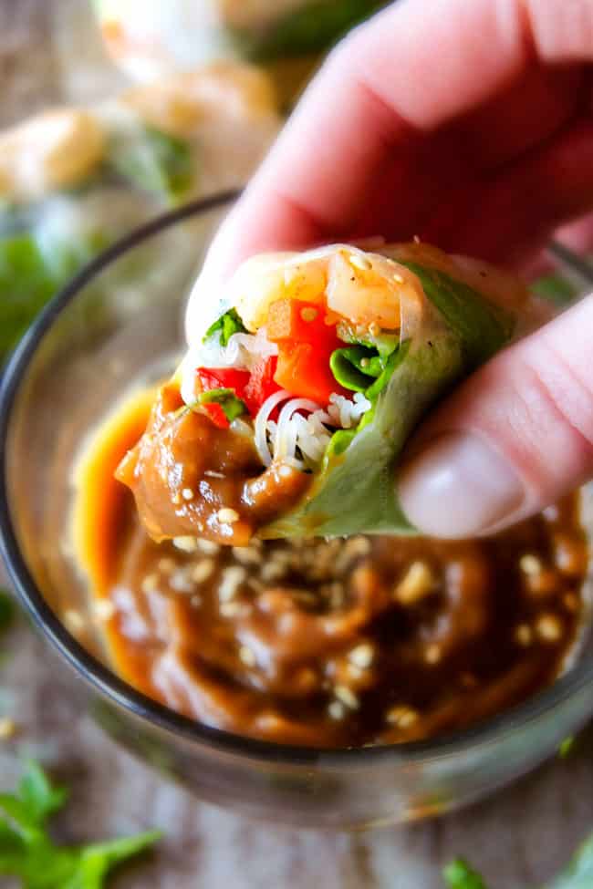 These insanely delicious Fresh Shrimp Spring Rolls are a flavor and texture explosion in every addictive bite and super easy to make with all my tips and tricks and step by step photos! and the the Pineapple Hoisin Peanut Sauce is EVERYTHING! up close of a hand holding a Vietnamese Spring Roll with peanut sauce