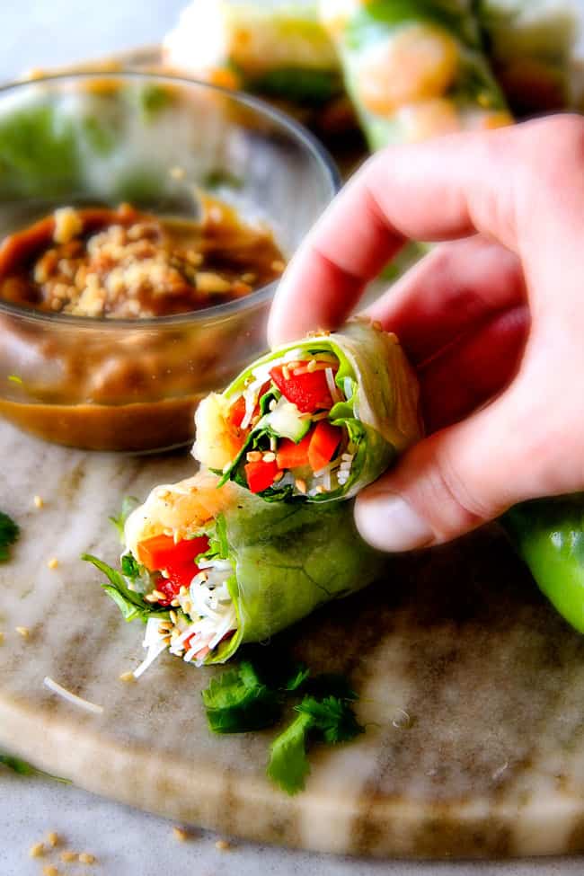 These insanely delicious Fresh Shrimp Spring Rolls are a flavor and texture explosion in every addictive bite and super easy to make with all my tips and tricks and step by step photos! and the the Pineapple Hoisin Peanut Sauce is EVERYTHING! a hand holding a fresh Vietnamese spring roll cut in half