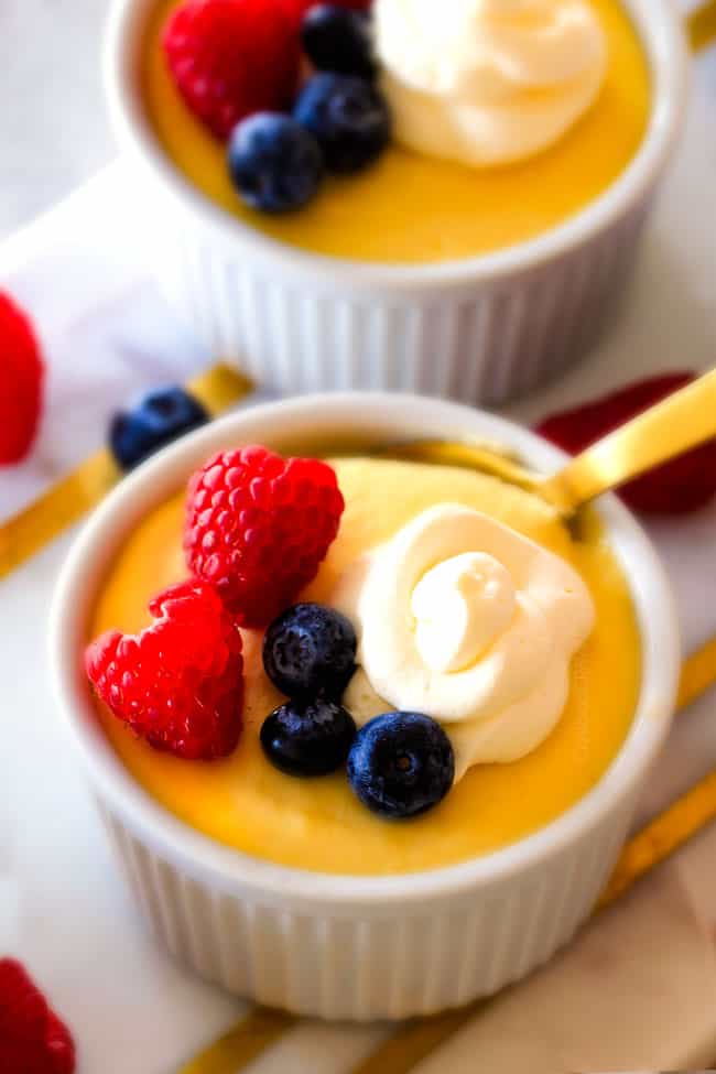 Lemon Pots de Creme with berries and cream on top with a gold spoon.