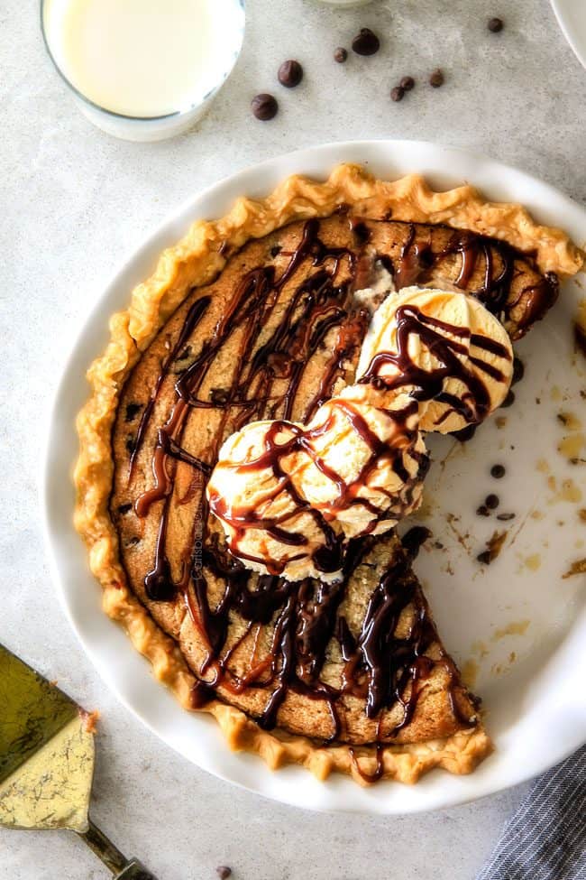 make ahead Million Dollar Cookie Pie layered with Nutella, Dulce de Leche and cookie dough! This is hands down the best skillet cookie I've ever made and its always such a crowd pleaser! top view of cookie pie with premade dough in a white pie pan, topped with ice cream, caramel and chocolate sauce