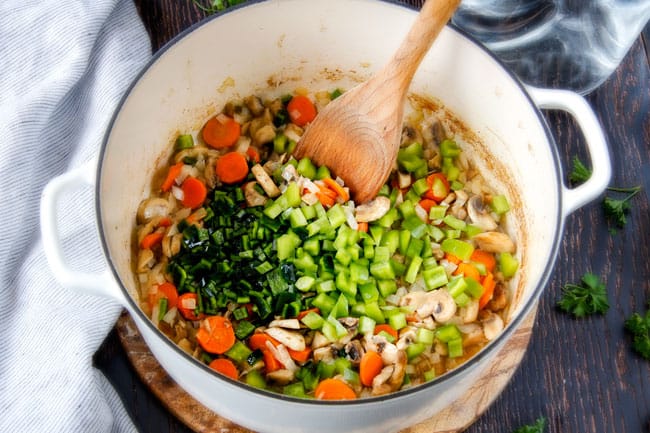 Showing how to make Philly Cheesesteak Soup by adding vegetables.