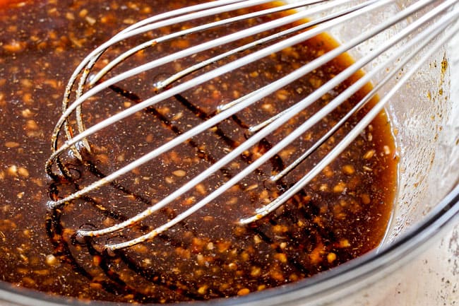 showing how to make korean beef bowls by whisking soy sauce, sesame oil, ginger, garlic, sugar and gochujang together in a glass bowl.