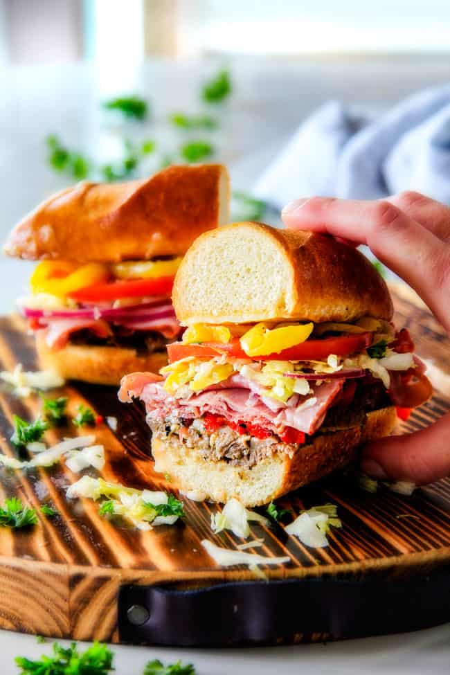 Easy, customizable LOADED Slow Cooker Italian Beef Sandwiches are crazy tender, seeping with flavor and unbelievably delicious! They make the easiest dinner or party food and super fun (make ahead!) sandwich bar! ย the best Italian Beef Sandwich sliced in half with a hand holding the sandwich