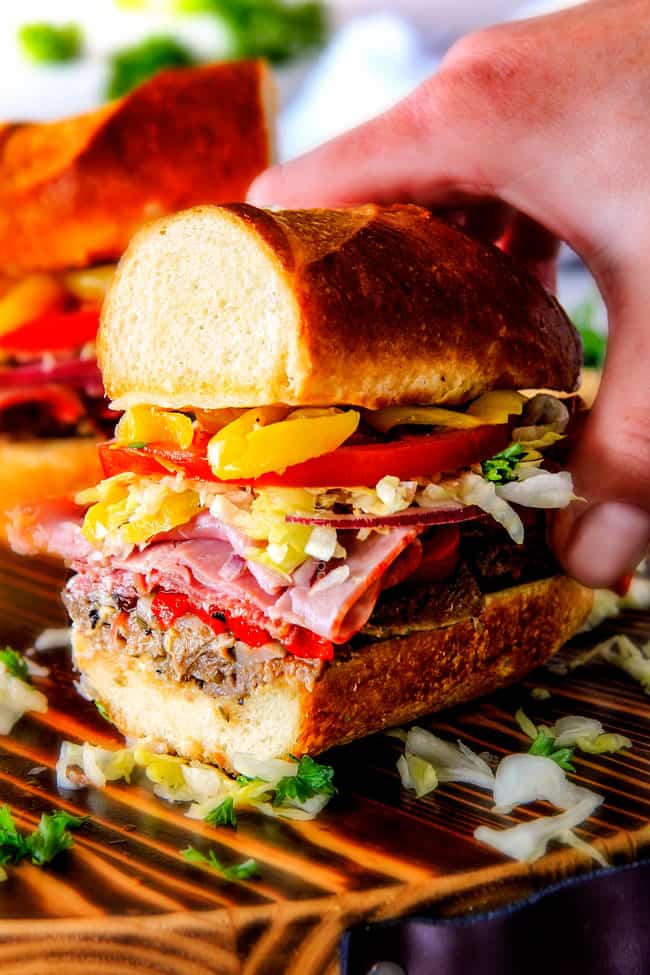 Easy, customizable LOADED Slow Cooker Italian Beef Sandwiches are crazy tender, seeping with flavor and unbelievably delicious! They make the easiest dinner or party food and super fun (make ahead!) sandwich bar! ย up close of a hand holding half of an easy Italian Sandwich