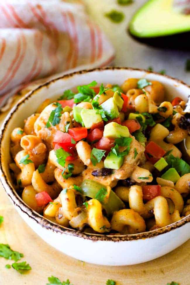 Lighter ONE POT Chicken Fajita Pastaย has only minutes of hands-on cooking time! ย Its smothered in cheesy, creamy salsa infused sauce bursting with your favorite fajita spiced chicken, onions and peppers! ย The pasta cooks right IN the sauce for simple prep, minimal cleanup, and extra flavooooor! ย a bowl of cheesy chicken fajita pasta garnished with avocados and tomatoes.