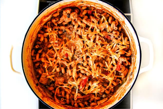 Lighter ONE POT Chicken Fajita Pastaย has only minutes of hands-on cooking time! ย Its smothered in cheesy, creamy salsa infused sauce bursting with your favorite fajita spiced chicken, onions and peppers! ย The pasta cooks right IN the sauce for simple prep, minimal cleanup, and extra flavooooor! ย showing how to make chicken fajita pasta by adding cheese and sour cream to the pot.