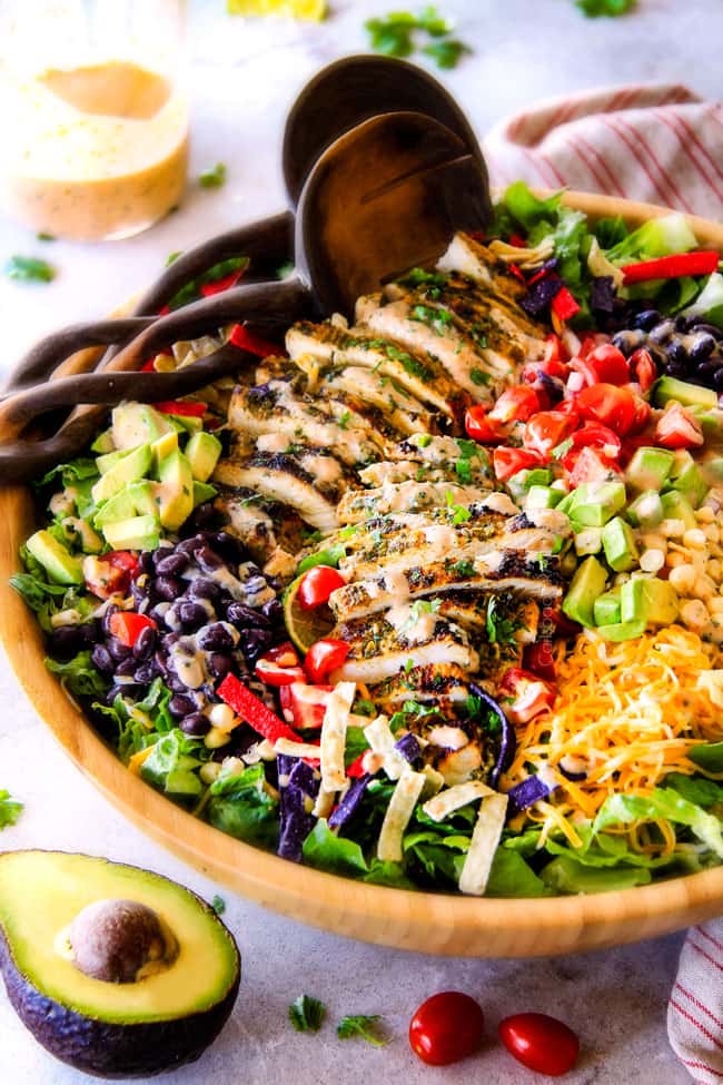 I couldn't stop eating this Cilantro Lime Chicken Taco Salad! ย Its bursting with tender, juicy chicken and the sweet & tangy Creamy Baja Catalina Dressing is out of this world delicious! ย This combo is pure heaven! side view of best chicken taco salad in a wood bowl with black beans, corn, tomatoes, avocados, cheese and tortilla strips