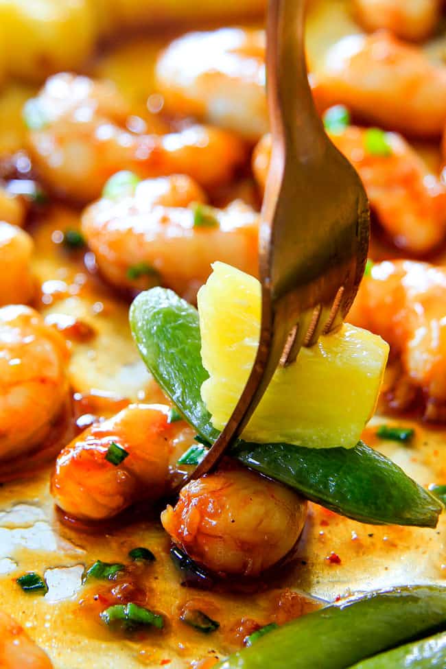 I am in love with this Sheet Pan Teriyaki Shrimp, Pineapple and Snap Peas! ย Its SO easy, healthy, a meal-in-one and the homemade Teriyaki sauce is the best I've ever had (DON'T be tempted to use store bought!)! ย I'm always keeping frozen shrimp on hand so I can make this any time!ย up close of a fork with teriyaki shrimp with the best homemade teriyaki sauce