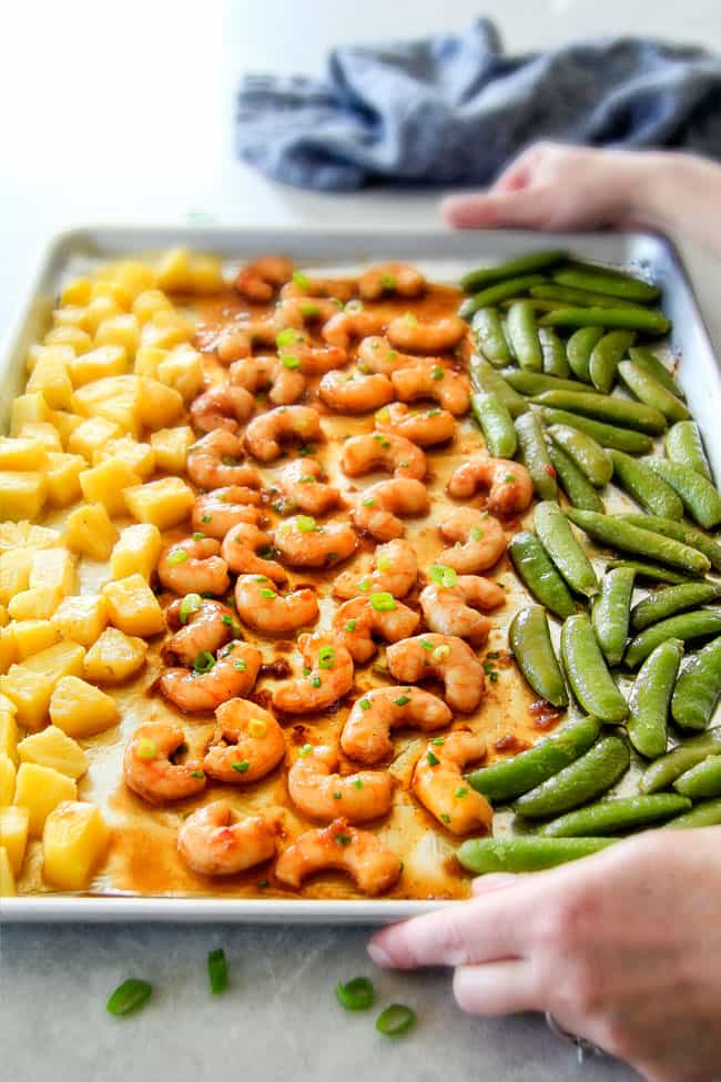 I am in love with this Sheet Pan Teriyaki Shrimp, Pineapple and Snap Peas! ย Its SO easy, healthy, a meal-in-one and the homemade Teriyaki sauce is the best I've ever had (DON'T be tempted to use store bought!)! ย I'm always keeping frozen shrimp on hand so I can make this any time!ย two hands holding a serving tray of easy teriyaki shrimp