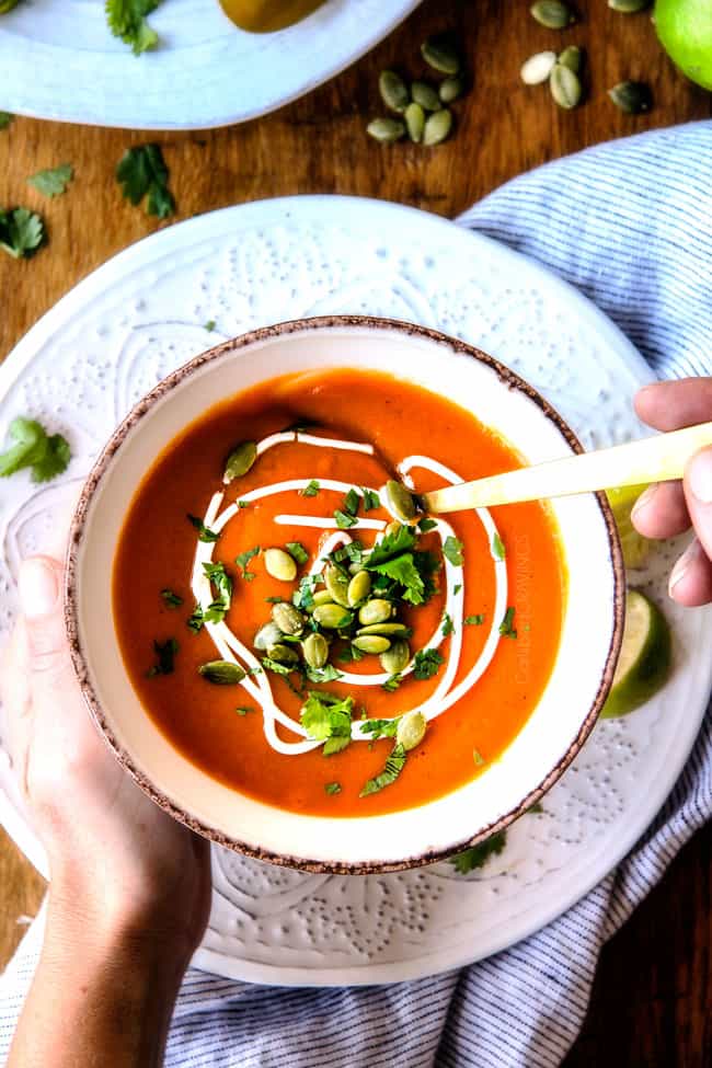 this SUPER creamy Slow Cooker Chipotle Sweet Potato Soup is AMAZING!ย Its loaded with flavor, gluten free, dairy free, crazy healthy and so easy!ย Definitely one of my new favorite soups!ย ย top view of two hands holding a bowl of savory Sweet Potato Soup