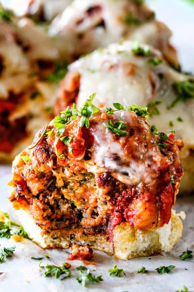 These Cheesy Italian Meatball Sliders are my favorite party food ever and my family loves them for dinner!ย The meatballs are the BEST (so tender and juicy!) and the marinara is amazing and I love how they are individual sliders instead of meatball subs!ย I can't recommend these enough!ย meatball slider on a Hawaiian roll with a bite taken out of it with cheese and marinara
