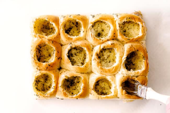 These Cheesy Italian Meatball Sliders are my favorite party food ever and my family loves them for dinner!ย The meatballs are the BEST (so tender and juicy!) and the marinara is amazing and I love how they are individual sliders instead of meatball subs!ย I can't recommend these enough!ย showing how to make meatball sliders by buttering the inside of Hawaiian rolls with butter, parsley and garlic