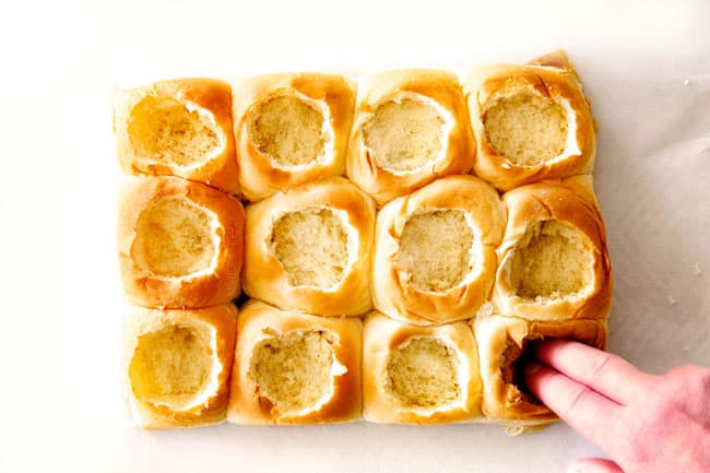 These Cheesy Italian Meatball Sliders are my favorite party food ever and my family loves them for dinner!ย The meatballs are the BEST (so tender and juicy!) and the marinara is amazing and I love how they are individual sliders instead of meatball subs!ย I can't recommend these enough!ย showing how to make meatball sliders by hollowing out Hawaiian rolls