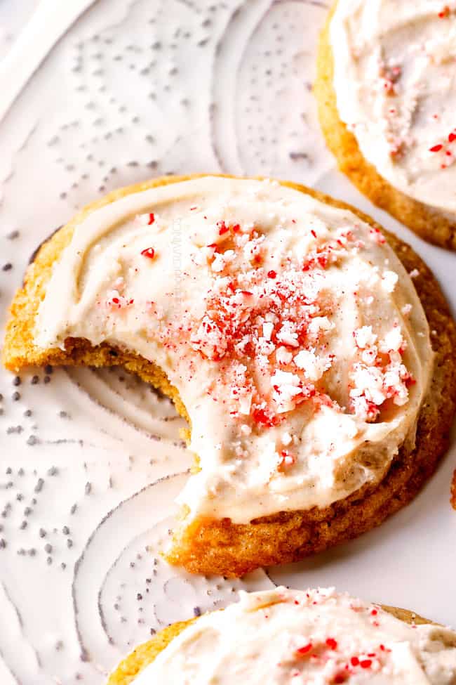 close up of an eggnog cookie topped with eggnog frosted and crushed candy canes. A bite is missing.