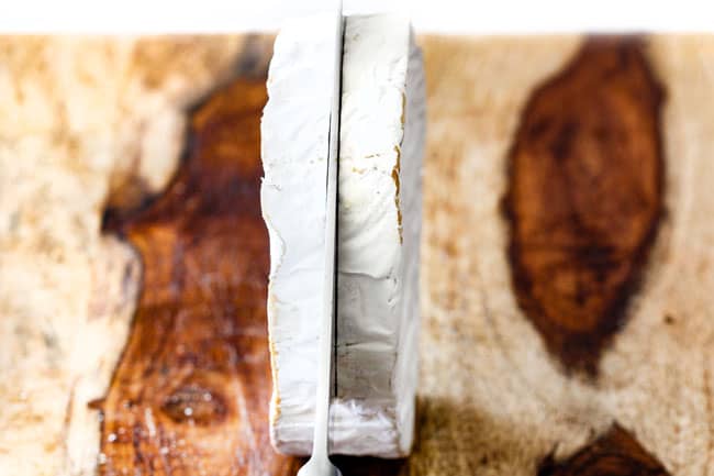 Rich and creamy Baked Brie in Puff Pastry is always a total luxuriously tasting crowd pleaser with minimal effort!ย (step by step pictures included)ย It can be prepped in advance then baked when you're ready for company!ย showing how to make baked brie in puff pastry by slicing brie down the center with a knife