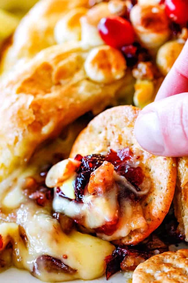 Rich and creamy Baked Brie in Puff Pastry is always a total luxuriously tasting crowd pleaser with minimal effort!ย (step by step pictures included)ย It can be prepped in advance then baked when you're ready for company!ย up close of oozing baked brie in puff pastry with jam, cranberries and pecans