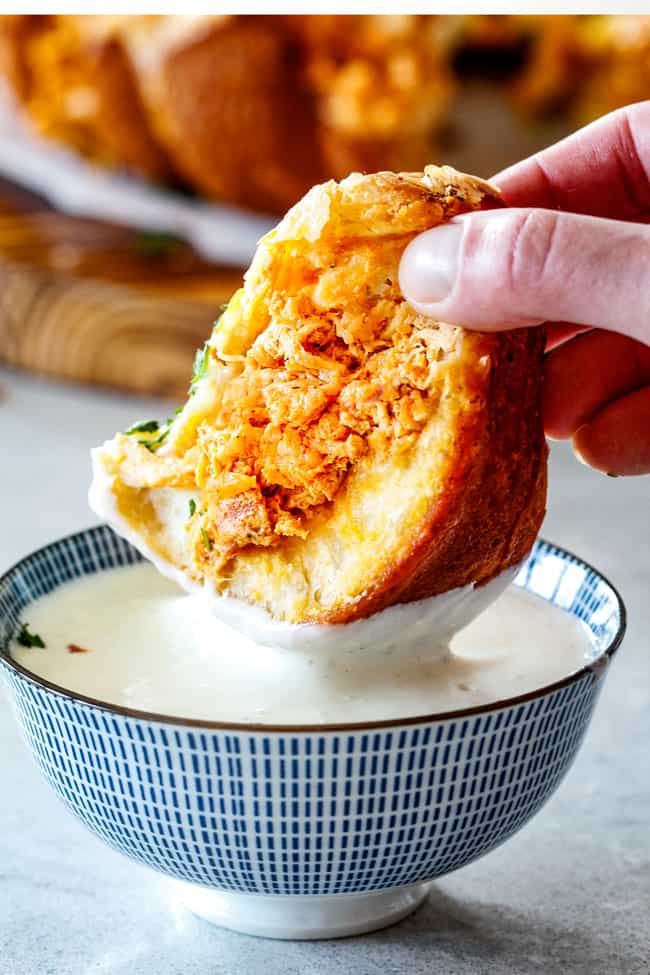 Mega flavorful Buffalo Chicken Pull Apart Bread is your favorite decadent creamy, cheesy dip baked right into a buttery biscuit ring! Crazy delicious EASY crowd pleasing appetizer perfect for parties or game day!ย ย It may look super impressive but you wonโt believe how easy it is! up close of dunking a piece of Buffalo Chicken Pull Apart Bread into blue cheese dressing