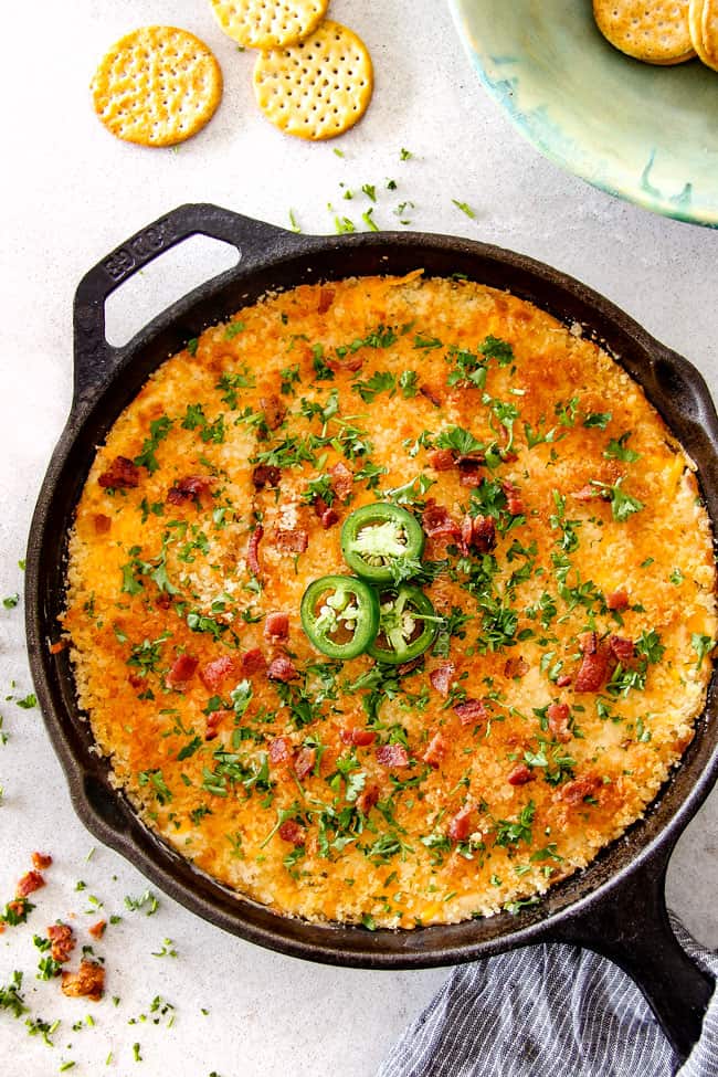 This quick and easy Jalapeno Popper Dip with Bacon tastes like your favorite appetizer in EASY, warm, creamy, cheesy addicting dip form!ย It is my go-to party appetizer that everyone LOVES!!!ย top view of Jalapeno Popper Dip with Bacon in a cast iron skillet with parsley and crackers