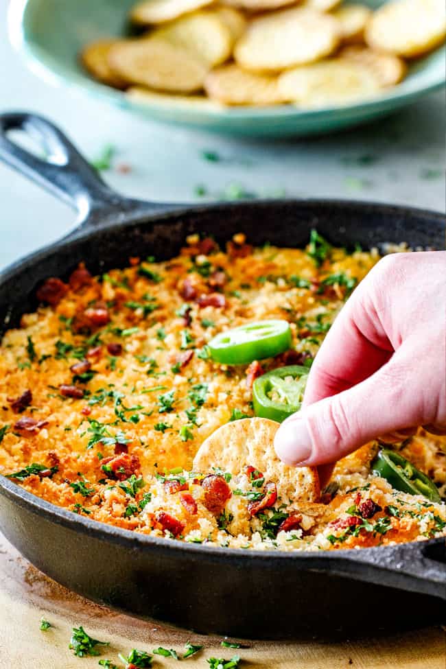 This quick and easy Jalapeno Popper Dip with Bacon tastes like your favorite appetizer in EASY, warm, creamy, cheesy addicting dip form!ย It is my go-to party appetizer that everyone LOVES!!!ย Far away shot of Bacon Jalapeno Popper Dip in a cast iron skillet with ritz crackers