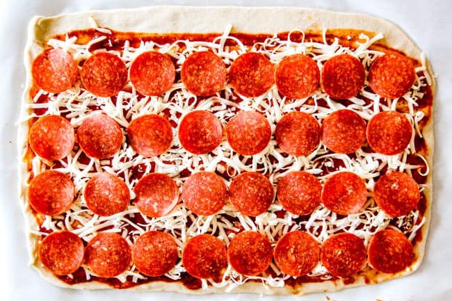 These Pizza Pinwheels are super easy to make, customizable, freeze beautifully, and absolutely irresistible for snacks, appetizers or fun meals! You friends and family will beg you to make these! showing how to make pizza pinwheels by adding layers of pepperoni