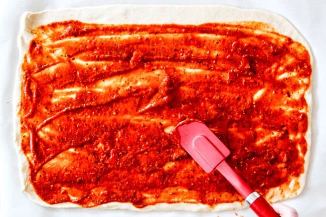 These Pizza Pinwheels are super easy to make, customizable, freeze beautifully, and absolutely irresistible for snacks, appetizers or fun meals! You friends and family will beg you to make these! showing how to make pizza pinwheels by spreading dough with marinara pizza sauce