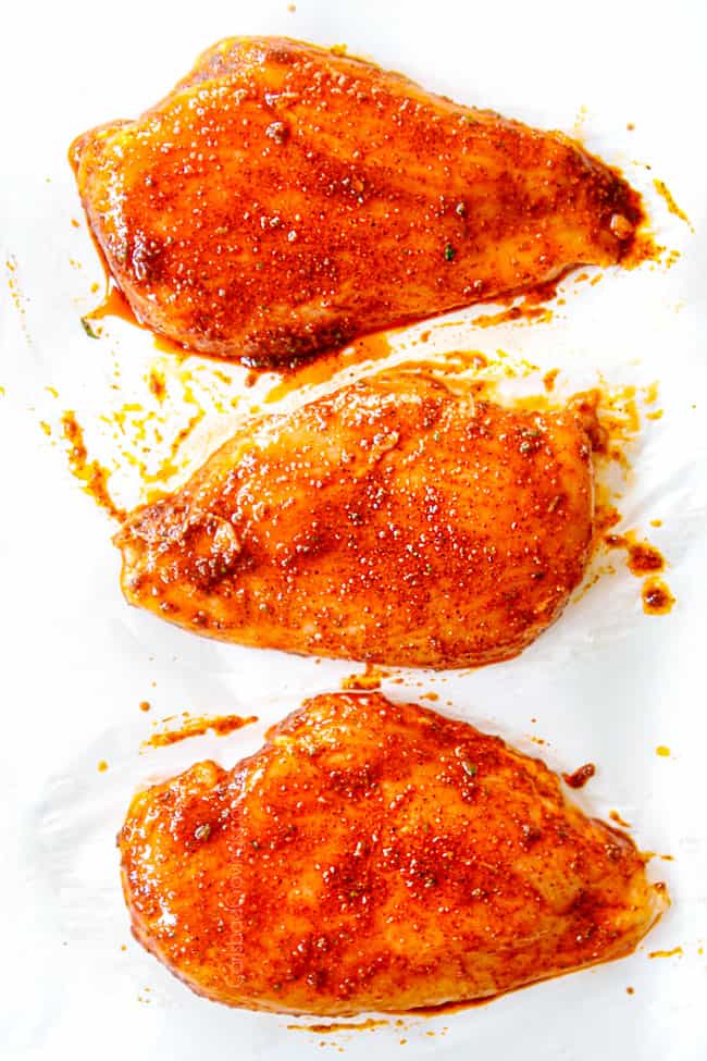 showing how to make Chili Lime Chicken by slathering 3 chicken breasts on parchment paper with the wet rub on pa