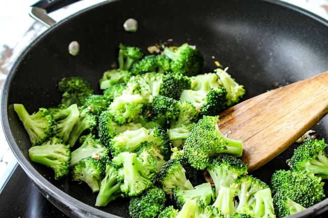 stir frying broccoli in a black skillet with garlic and ginger showing how to make beef and broccoli