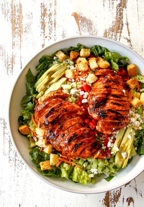 top view of Buffalo Chicken Salad in a white bowl with best buffalo chicken, blue cheese, celery, carrots, avocado, red bell peppers and lettuce