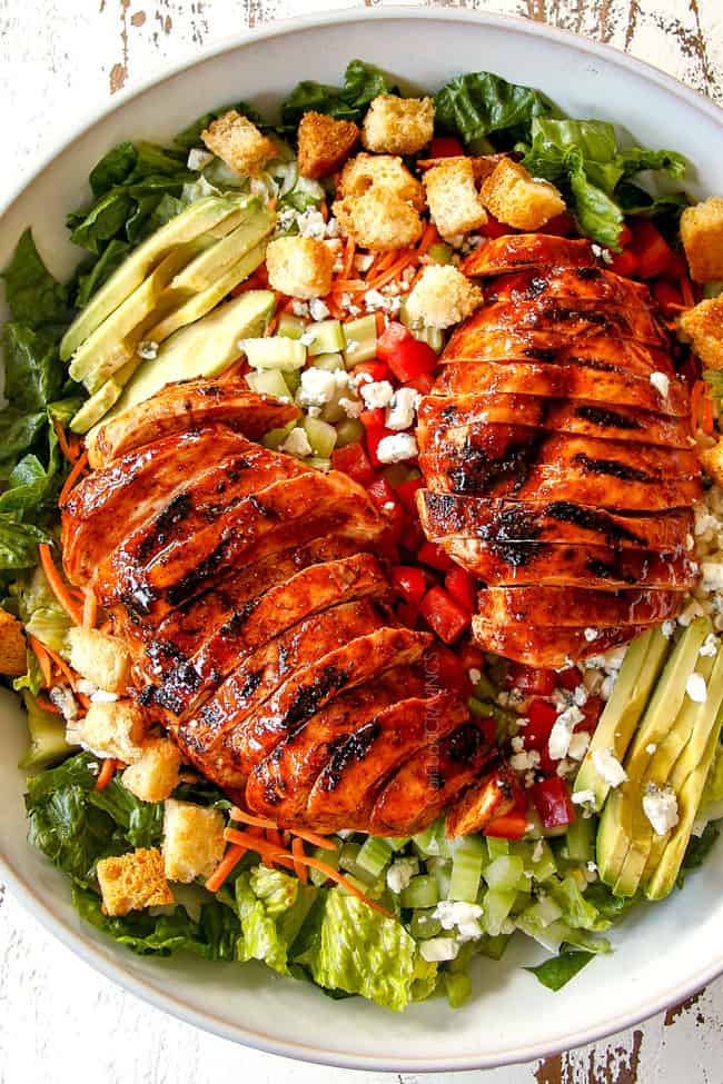 top view of Buffalo Chicken Salad in a white bowl with best buffalo chicken, blue cheese, celery, carrots, avocado, red bell peppers and lettuce