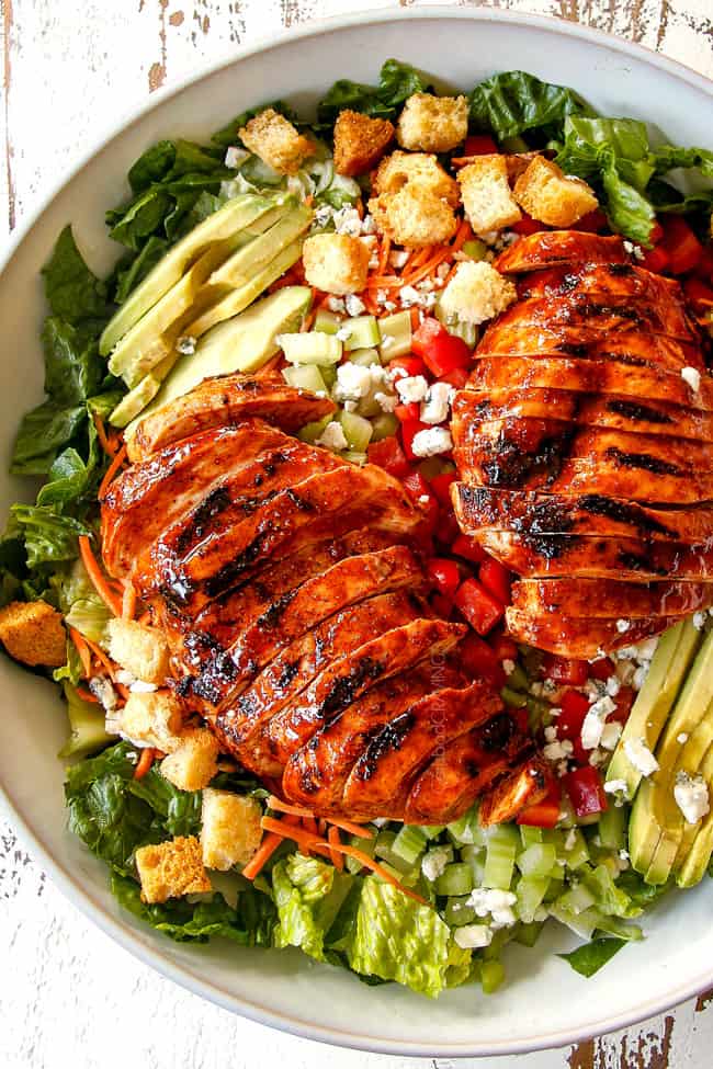 top view of Buffalo Chicken Salad in a white bowl with best buffalo chicken, blue cheese, celery, carrots, avocado, red bell peppers and lettuce