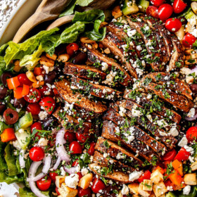 top view of Greek Chicken Salad with yogurt dressing in a white bowl with tomatoes, olives, cucumber, red onions and Greek Chicken