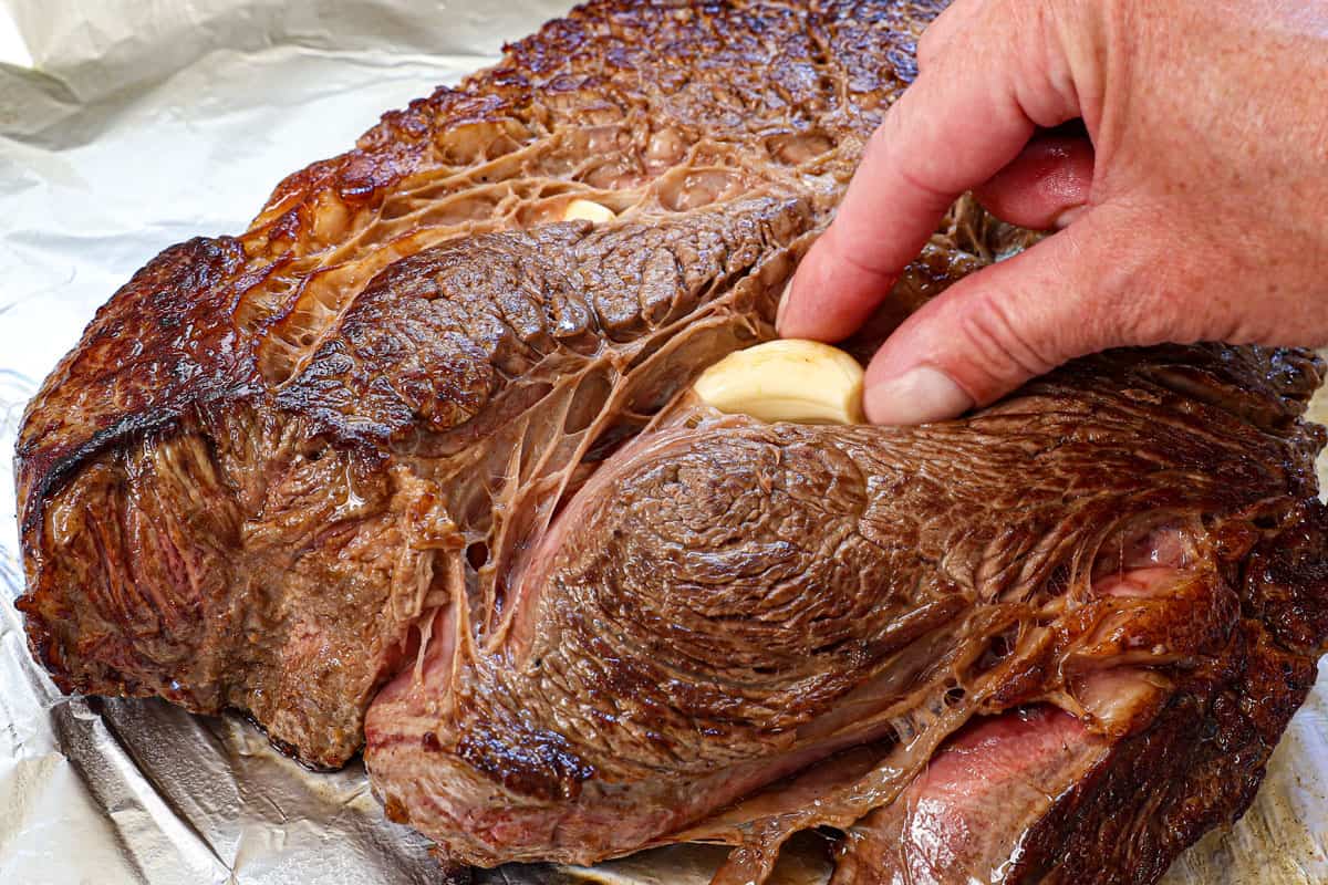 showing how to cook a roast in the oven by adding whole garlic cloves in the fat crevices