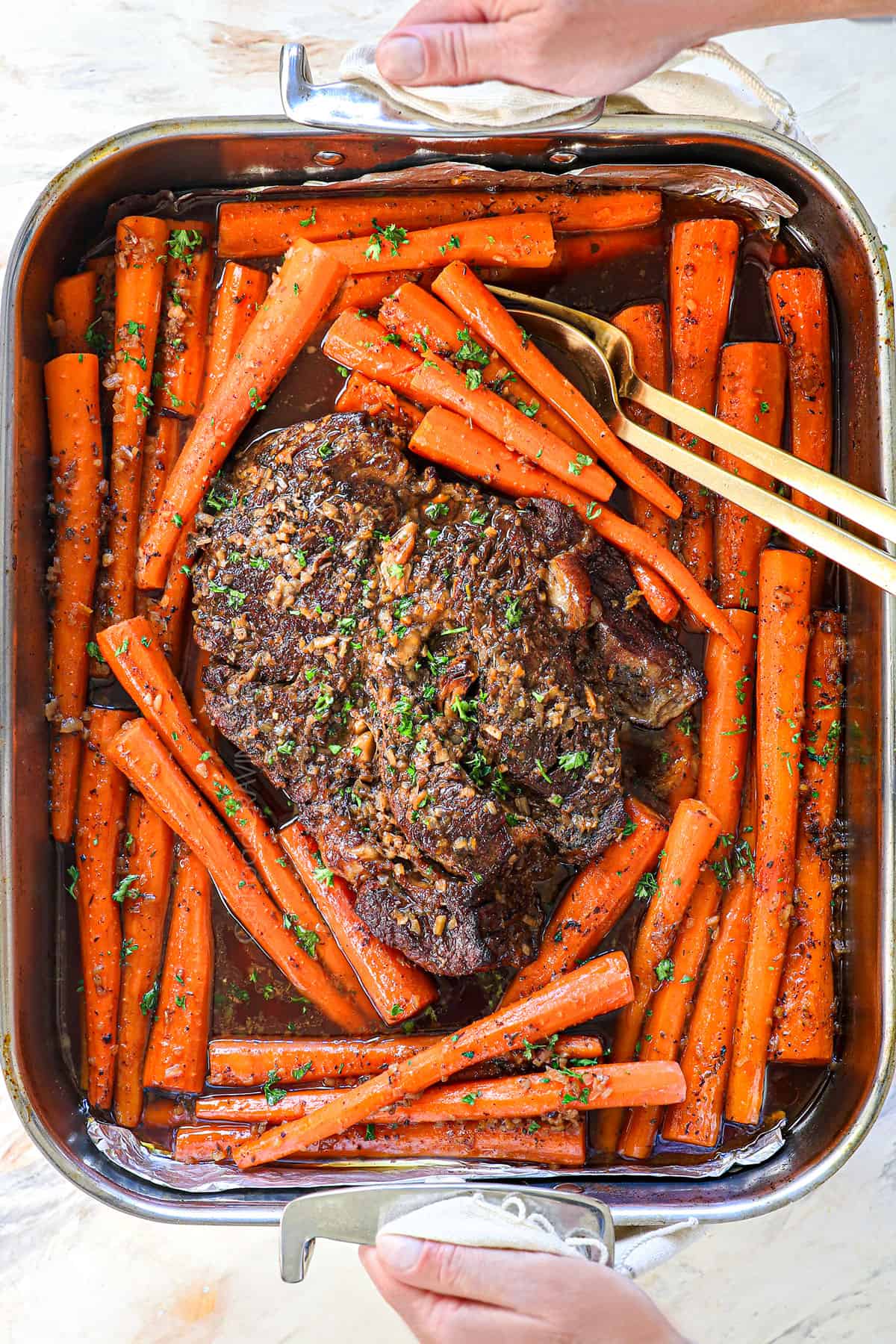 holding the roast in a pan surrounded by carrots that's just come out of the oven