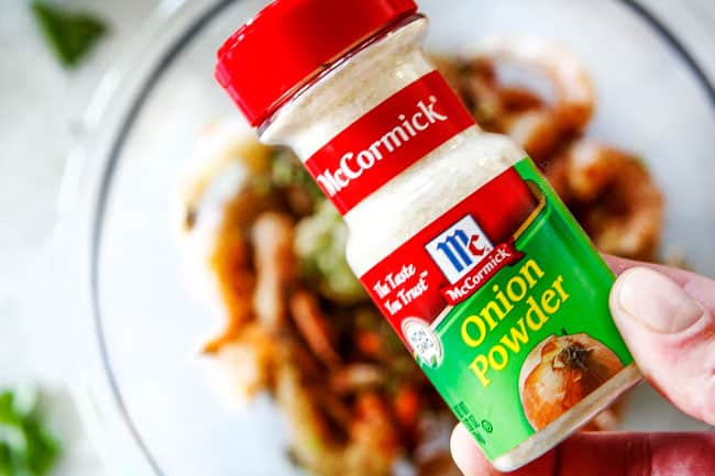 Cilantro Lime Shrimp Tacos EXPLODING with tangy, punchy flavor complimented by sweet refreshing Mango Salsa and silky Avocado Crema on your table in 35 minutes!ย You can prep the toppings ahead of time for a super quick and easy weeknight dinner that tastes better than any restaurant! showing how to make shrimp tacos by adding raw shrimp to a bowl with onion powder, garlic, paprika, ground cumin, for healthy Shrimp Tacos