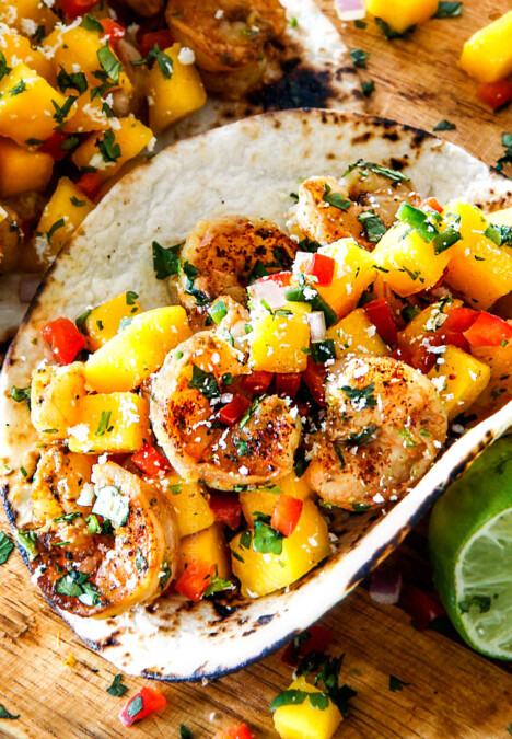 Cilantro Lime Shrimp Tacos with Mango Salsa and Avocado lined in a row on a brown cutting board