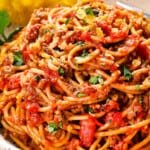 showing how to serve cheesy taco spaghetti by topping with cilantro and tortilla chips in a bowl