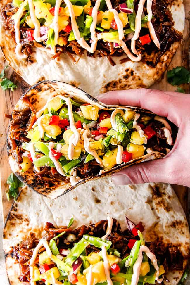 Top shot of picking up a pulled pork taco on a cutting board