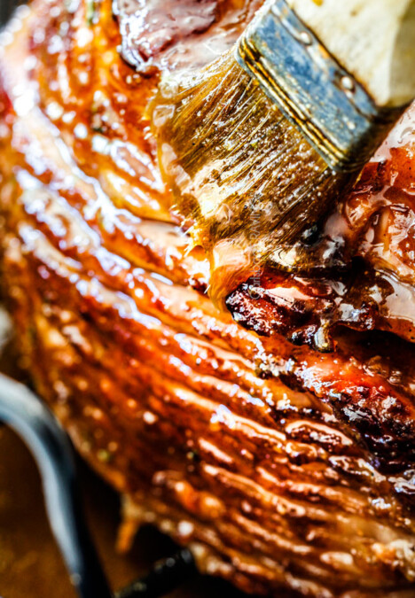 Brown Sugar Glazed Ham on a white platter being brushed with brown sugar glaze for ham