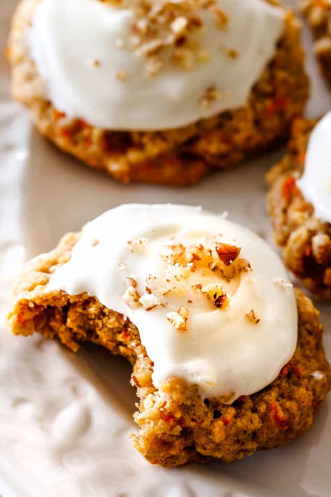 Up close of soft Carrot Cake Cookies with Cream Cheese Frosting with a bite taken out of it on a white plate