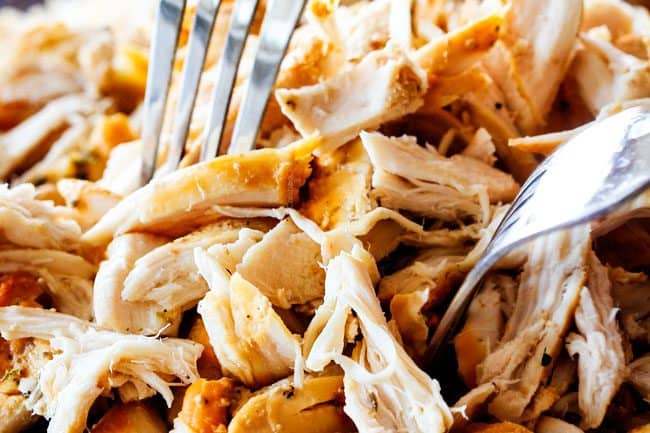showing how to make Chicken Enchilada Soup recipe by shredding chicken on a cutting board with two forks