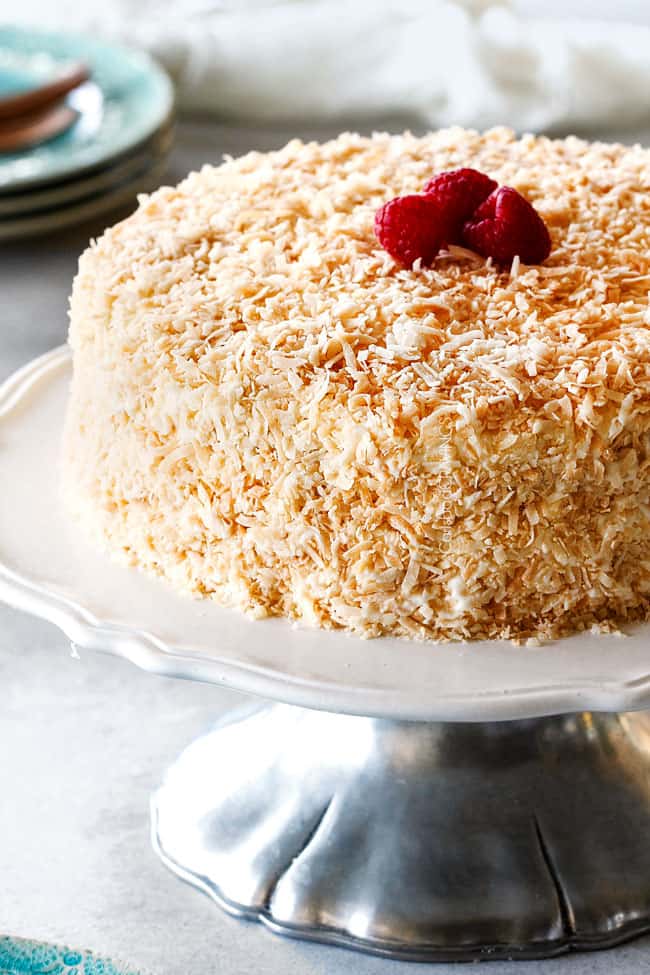 Best Coconut Cake on a white cake stand with toasted coconut