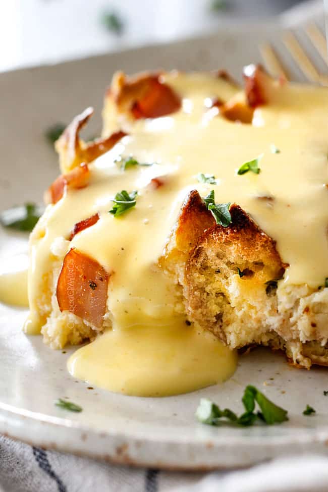 up close shot of Eggs Benedict Casserole on a speckled plate being smothered by Hollandaise Sauce