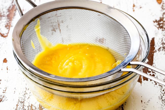 Showing how to make Lemon Curd for Lemon Blueberry Cake by straining lemon curd in a fine mesh sieve over a glass bowl
