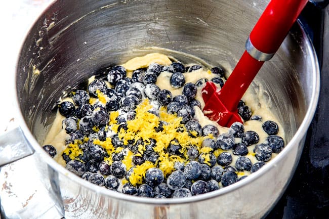 Showing how to make Lemon Blueberry Cake by adding blueberries and lemon zest to large metal mixing bowl with batter