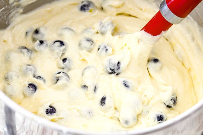 Showing how to make Lemon Blueberry Cake with Lemon Curd by gently mixing blueberries into batter with red spatula