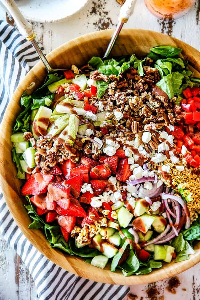 top shot of easy Strawberry Salad with Poppy Seed Dressing with strawberries, goat cheese, pecans, red onion in a wood bowl with white tongs