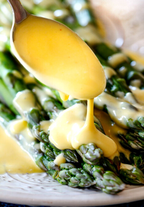 Spooning rich and creamy Blender Hollandaise Sauce on asparagus on a white platter