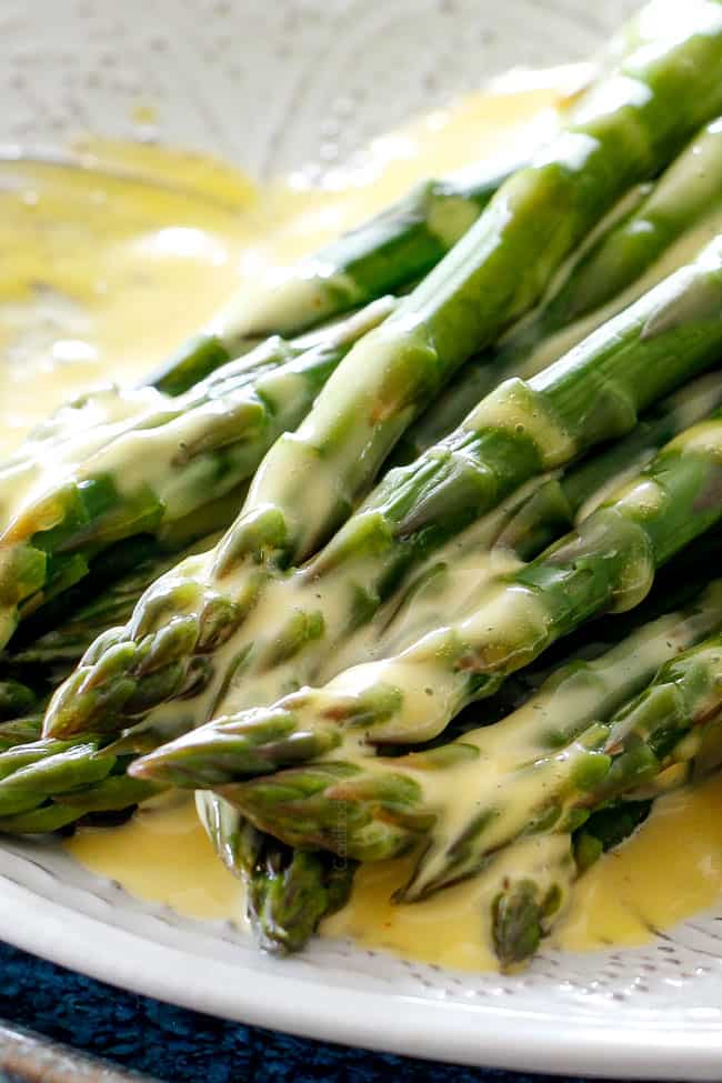 Up close shot of asparagus on a white platter that has been drizzled with easy Blender Hollandaise Sauce